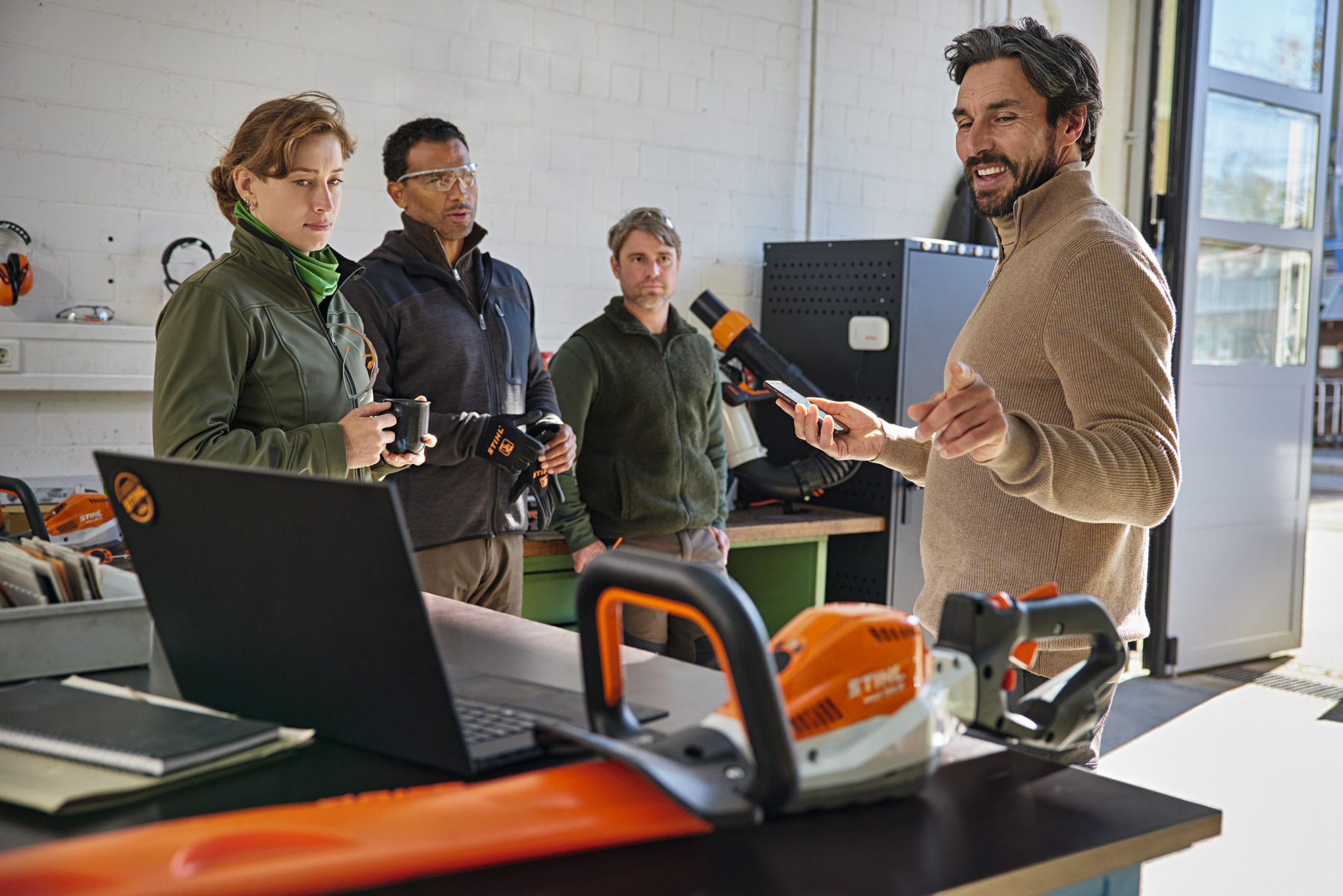 Quattro persone all'interno di un'officina e una che illustra l'app STIHL connected su uno smartphone